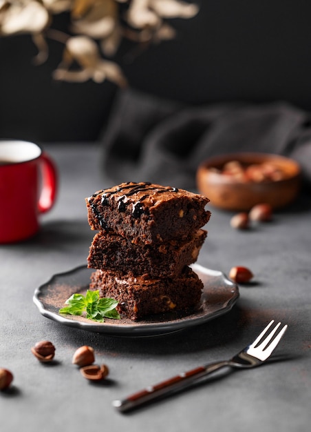 Een stapel chocolade brownies met munt en hazelnoten op een donkere achtergrond met een kop koffie en noten