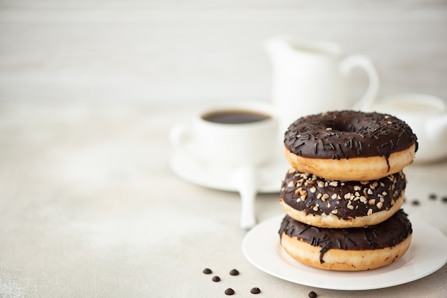 Een stapel chocolade geglazuurde donuts met koffie en melk op een witte tafel