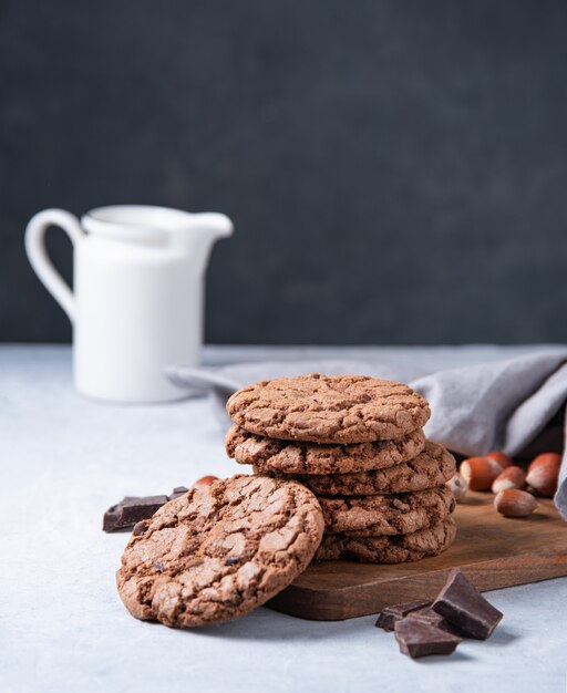 Een stapel chocoladeschilferkoekjes met chocoladeschilfers en noten met kruik op een lichte lijst. Vooraanzicht en kopieerruimte