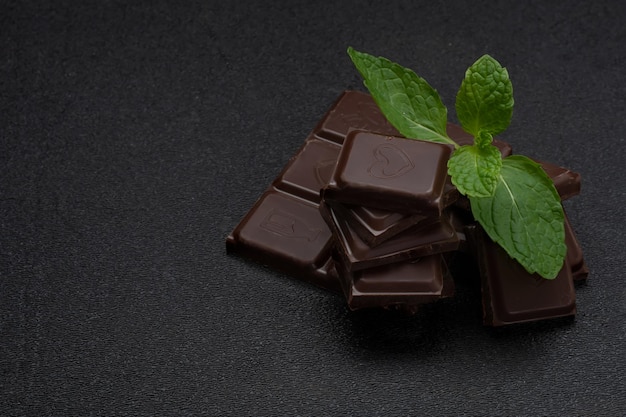 Een stapel donkere chocoladerepen met een groen blad bovenop zwarte achtergrond