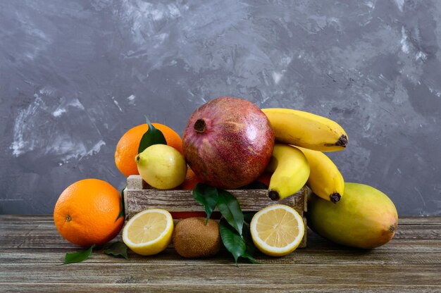 Een stapel exotisch fruit (bananen, sinaasappels, kiwi, granaatappel, mango, guave, citroen) in een houten kist op tafel.