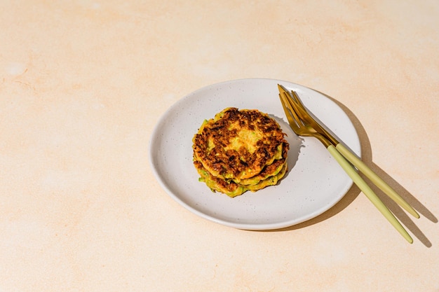 Een stapel gebakken groentepannenkoekjes gemaakt van courgette en wortel geschoten met hard licht met schaduwen geserveerd op een bord met gouden mes en vork