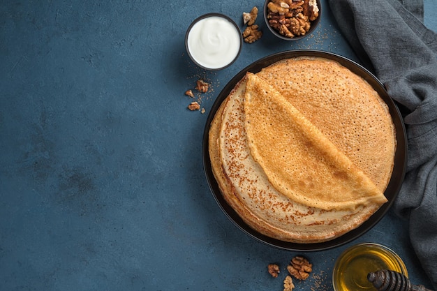 Een stapel gebakken pannenkoeken op een donkere achtergrond met boter, honing en zure room. Maslenitsa, Russische blini. Bovenaanzicht.