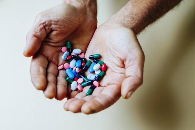 Een stapel gekleurde tabletten en pillen ligt in de seniele hand van onherkenbare medicijnen