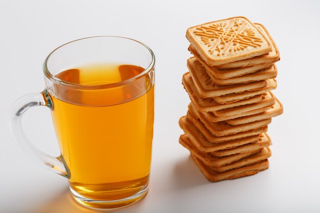 Een stapel gouden tarwekoekjes en een mok geurige groene thee op grijs