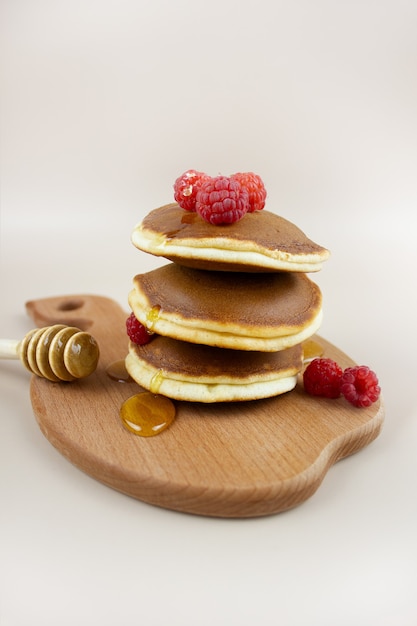 Een stapel heerlijke zelfgemaakte pannenkoeken met frambozen, gegoten met honing en een lepel op een houten dienblad.