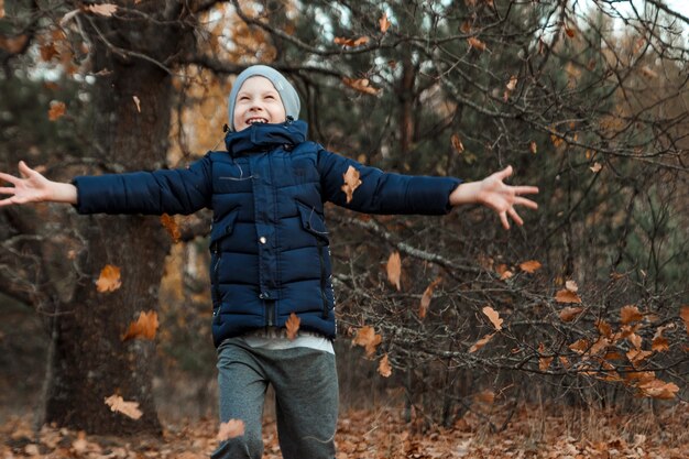 Een stapel herfst, geel gebladerte, een kind, een jongen die met gebladerte in een park speelt, werpt bladeren op.