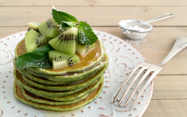 Een stapel pannekoeken met stroop en kiwi.