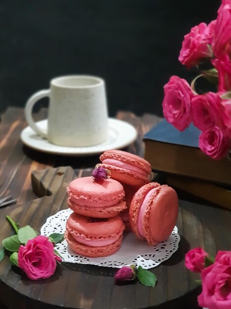 Een stapel roze bitterkoekjes staat op een tafel met een boek en een kopje koffie.