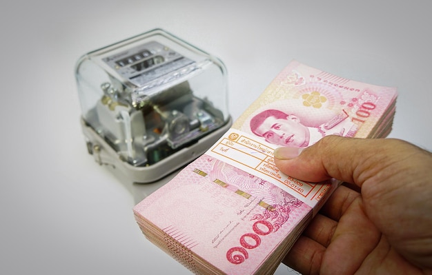 Een stapel van honderd baht-bankbiljetten met elektriciteitsmeter Betaal voor elektriciteit