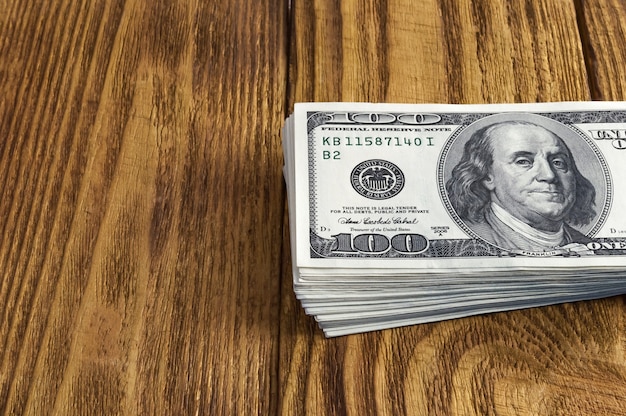 Een stapel van honderd dollar Amerikaanse bankbiljetten gegooid op een houten tafel.