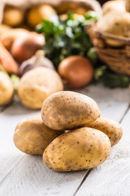 Een stapel verse aardappelen en assortiment groenten op de achtergrond.