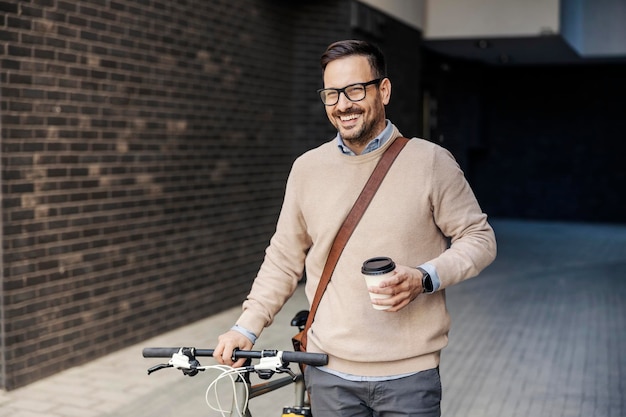 Een stedelijke zakenman duwt zijn fiets op straat en geniet van afhaalkoffie