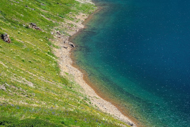 Een steile groene berghelling boven een turquoise helder bergmeer. Natuurlijke milieuvriendelijke achtergrond.