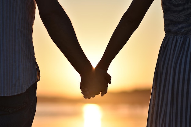 Foto een stel dat elkaar de hand houdt op het strand tegen de hemel tijdens de zonsondergang