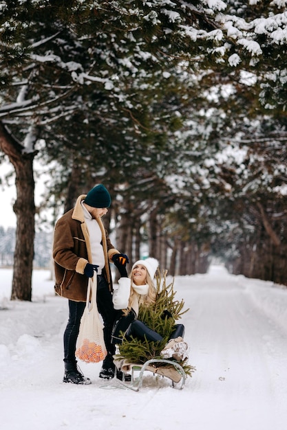 Een stel dat plezier heeft met een slee in een kerstboombos, mandarijnen eet en geniet van een sneeuw