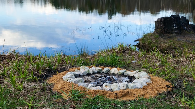 Een stervend kampvuur aan de oever van een meer in het bos op een lentedag