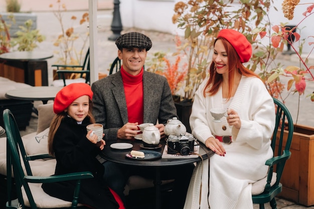 Een stijlvol gezin verzameld in een café op straat Moeder, vader, dochtertje, drinkt thee, eet gebak Ze zijn samen gelukkig Het concept van een gelukkig familiediner