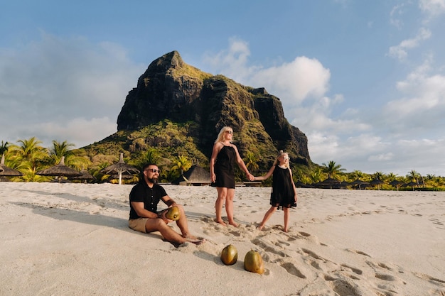 een stijlvolle familie in zwarte kleding met kokosnoten in hun handen op het strand van het eiland Mauritius. Mooie familie op het eiland Mauritius in de Indische Oceaan.