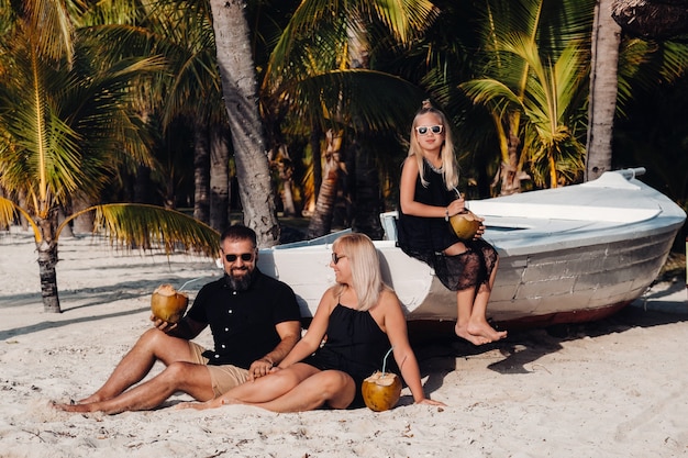 Een stijlvolle familie in zwarte kleding met kokosnoten in hun handen op het strand van het eiland Mauritius. Mooie familie op het eiland Mauritius in de Indische Oceaan.