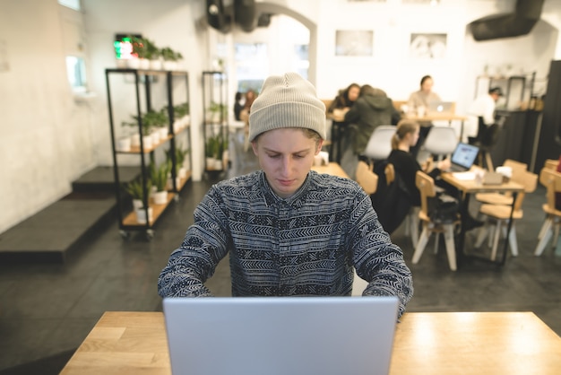 Een stijlvolle freelancer werkt voor een laptop in een gezellig café. Een student zit aan een cafe tafel en met behulp van een laptop