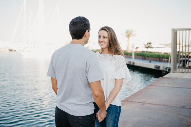 Een stijlvolle jongeman houdt handen vast met zijn brunette vriendin in de haven