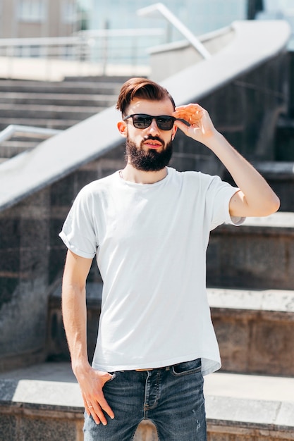 Een stijlvolle jongeman met een baard in een wit T-shirt en bril