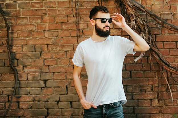 Een stijlvolle jongeman met een baard in een wit T-shirt en bril