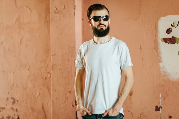 Een stijlvolle jongeman met een baard in een wit T-shirt en bril