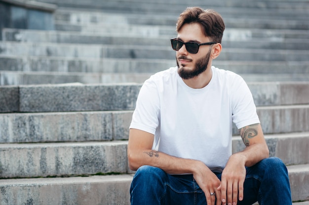 Een stijlvolle jongeman met een baard in een wit t-shirt en een bril