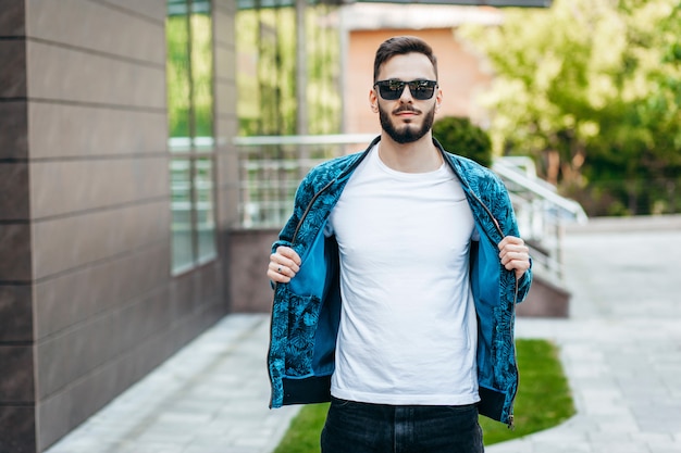 Een stijlvolle jongeman met een baard in een wit t-shirt en zonnebril