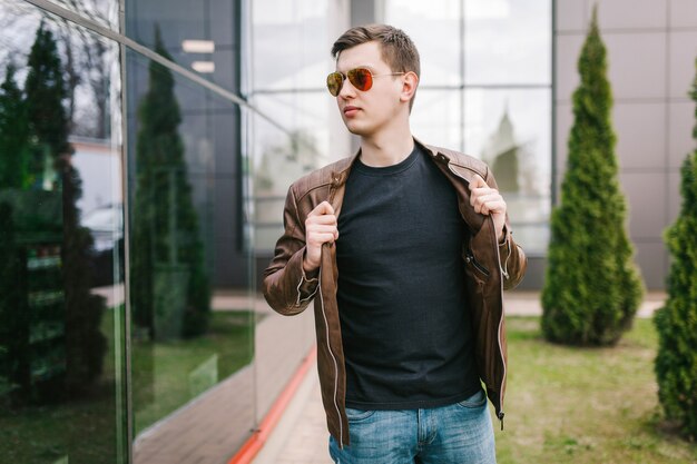 Een stijlvolle man in leren jas, bril en zwart T-shirt. Straatfoto