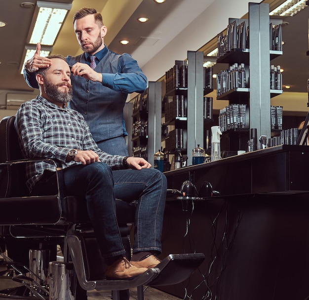 Een stijlvolle Meester-kapper doet een knipbeurt bij de klant. Herenkapsel in een kapperszaak. Haar stylen met een kam.