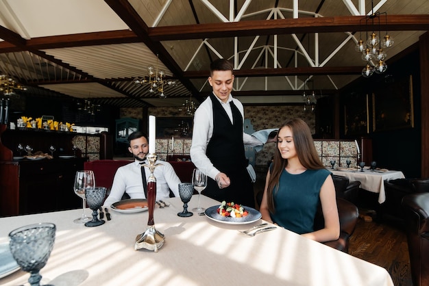 Een stijlvolle ober bedient een jong stel van een man en een vrouw die op een date naar een gastronomisch restaurant kwamen Klantenservice in het restaurant en horecagelegenheden