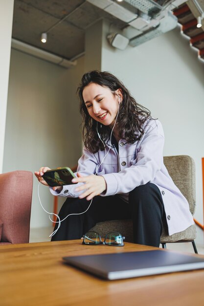 Een stijlvolle vrouw met een bril in een modern café aan een tafel met een telefoon werkt online Een vrouw praat aan de telefoon via een koptelefoon Werk op afstand Werk van een freelancer