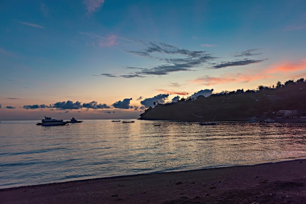 Een strand bij zonsondergang met een paar boten in het water