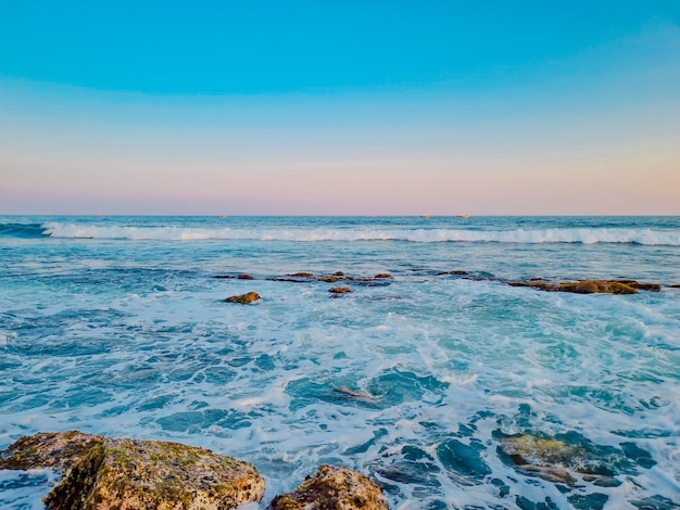 Een strand met rotsen en water met een blauwe lucht op de achtergrond