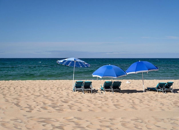 Een strandscène met een blauwe paraplu en stoelen op het zand.