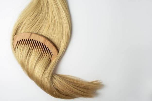 Een streng blond haar met een houten kam erop liggend op een witte achtergrond