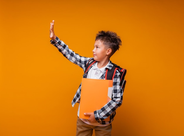 Een student begroet op een gele achtergrond het portret van een jongen met een rugzak en een map