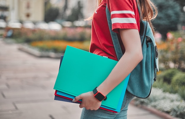 Een student in een rood T-shirt met een rugzak en gekleurde blocnotes in haar hand, de backplane van het stadsplein