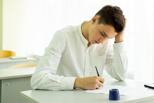 Een student maakt aantekeningen met een vulpen terwijl hij op de middelbare school studeert terwijl hij aan een bureau zit