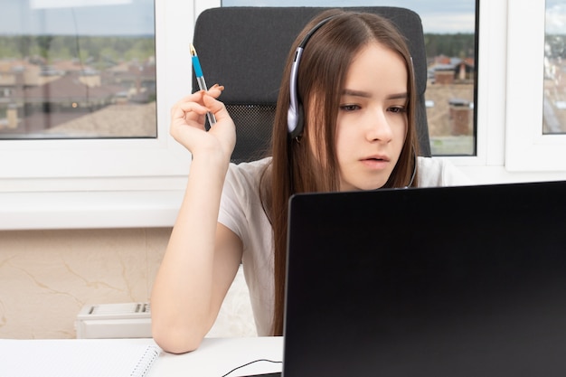 Een student thuis is bezig met trainen, luistert aandachtig en kijkt naar een college op een laptop met een microfoon in koptelefoon