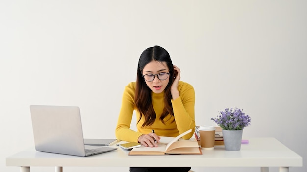 Een studente met een bril is gefocust op haar huiswerk en werkt aan haar bureau