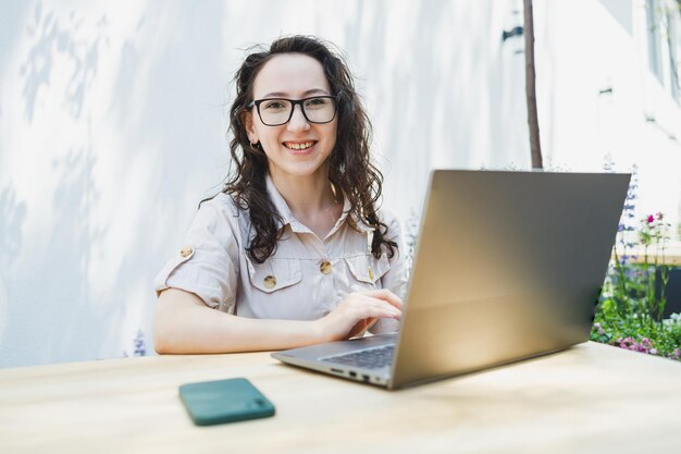 Een studente zit op het zomerterras van een café en werkt op een laptop Vrouwelijke freelancer werkt op afstand online terwijl ze in een zomercafé zit Werken op afstand