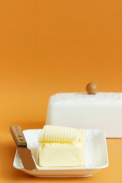 Een stuk boter in botervloot en een mes op een gekleurde achtergrond. Selectieve aandacht.