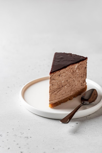 Een stuk chocolade cheesecake op een witte plaat met een lepel op een witte achtergrond Tekstruimte