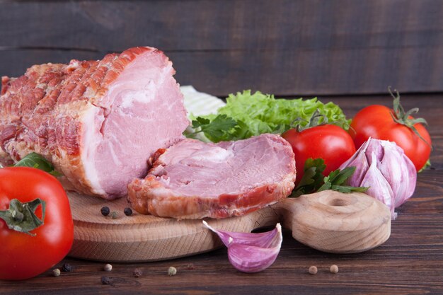 Een stuk ham en groenten op een houten achtergrond. Vleeswaren product