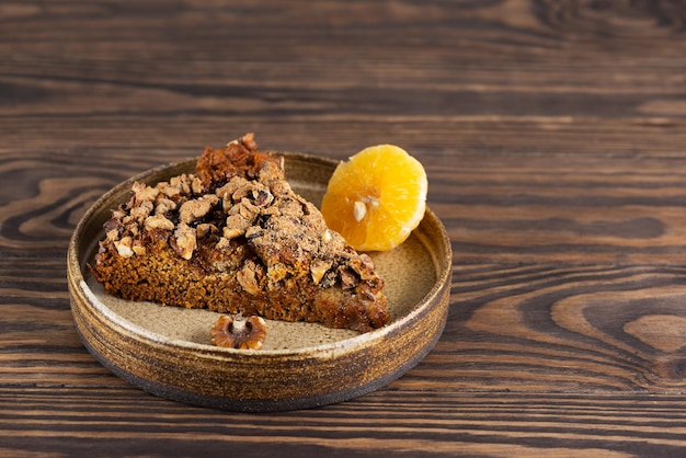 Een stuk mandarijntaart met walnoten in een bord op een houten tafel Suikergluten- en lactosevrij