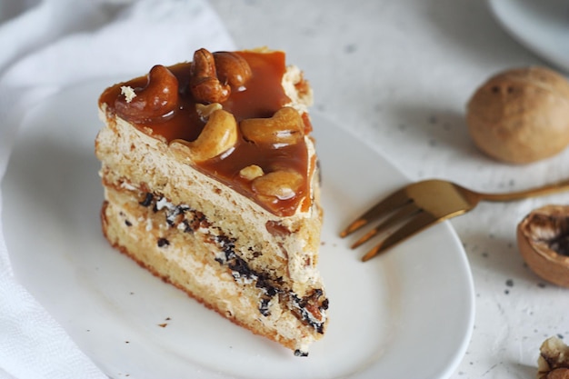 Een stuk notencake zit in een bord op een lichttafel. Vlakbij liggen een gouden vork, noten en een handdoek